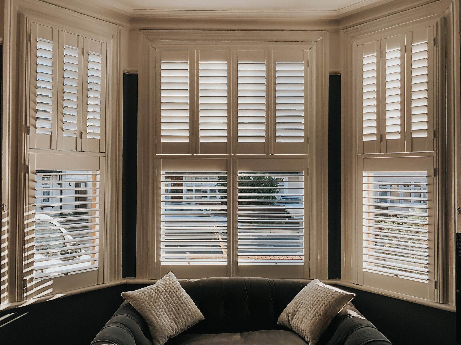 Taupe shutters around a bay window seat with cushions