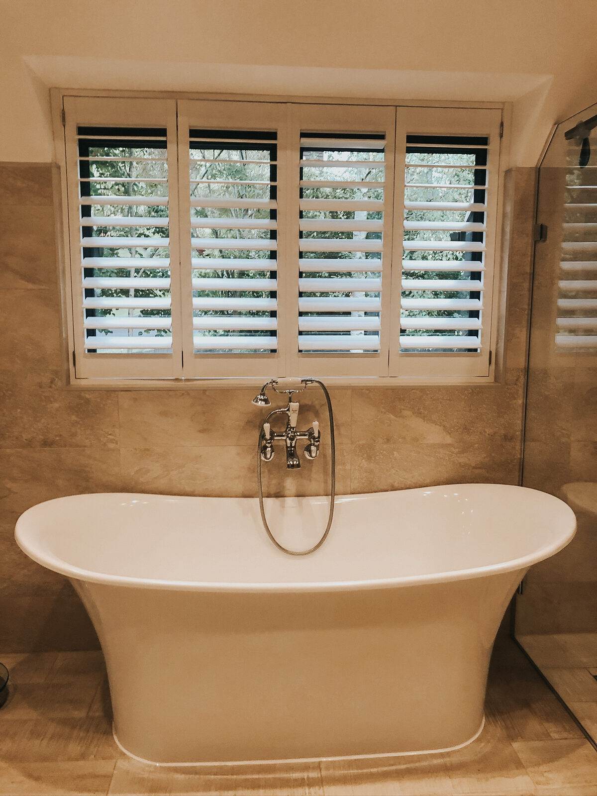 Shutters above a freestanding bath in a stone bathroom