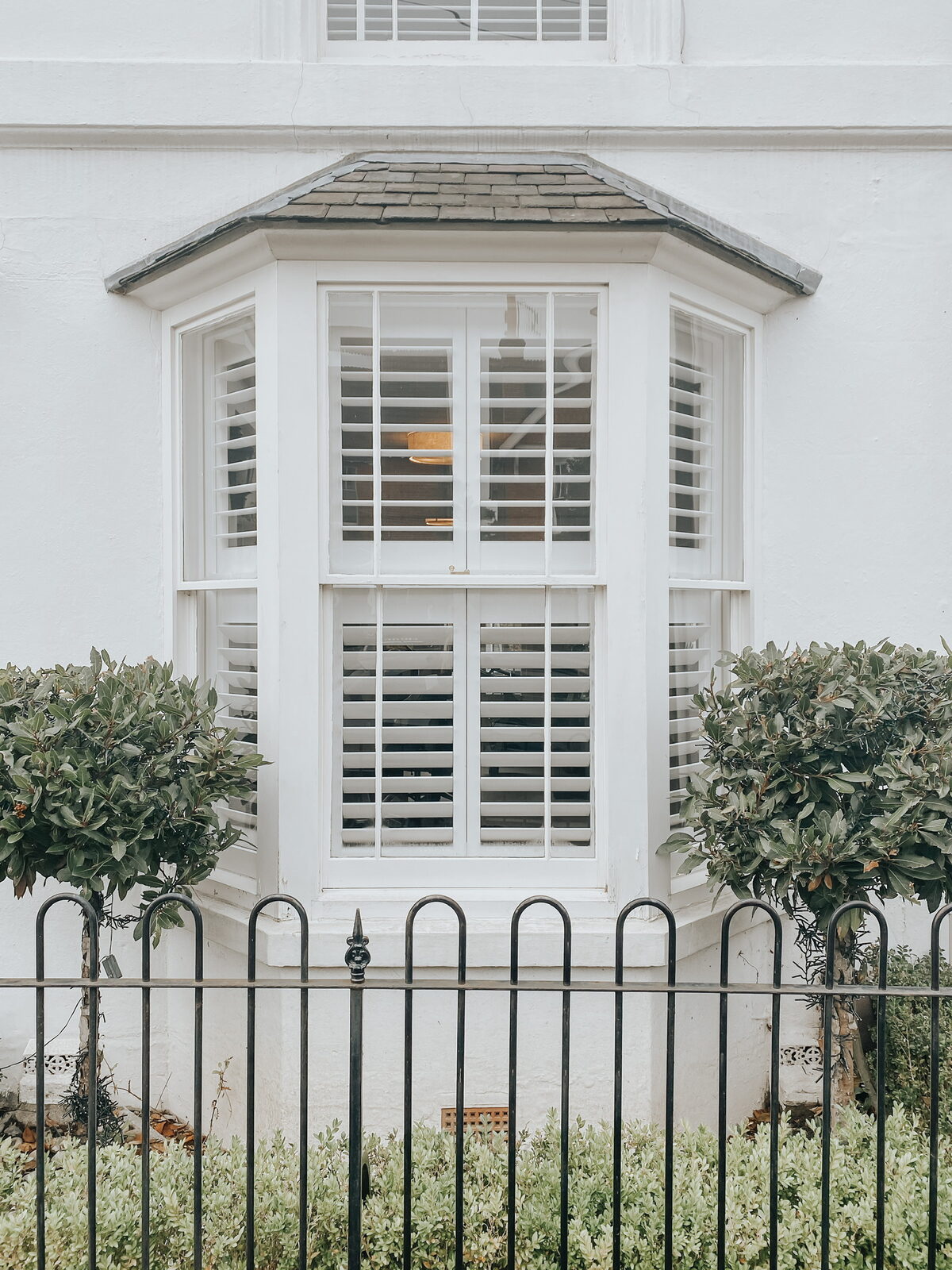 Victorian bay window fitted with white shutters seen from the street