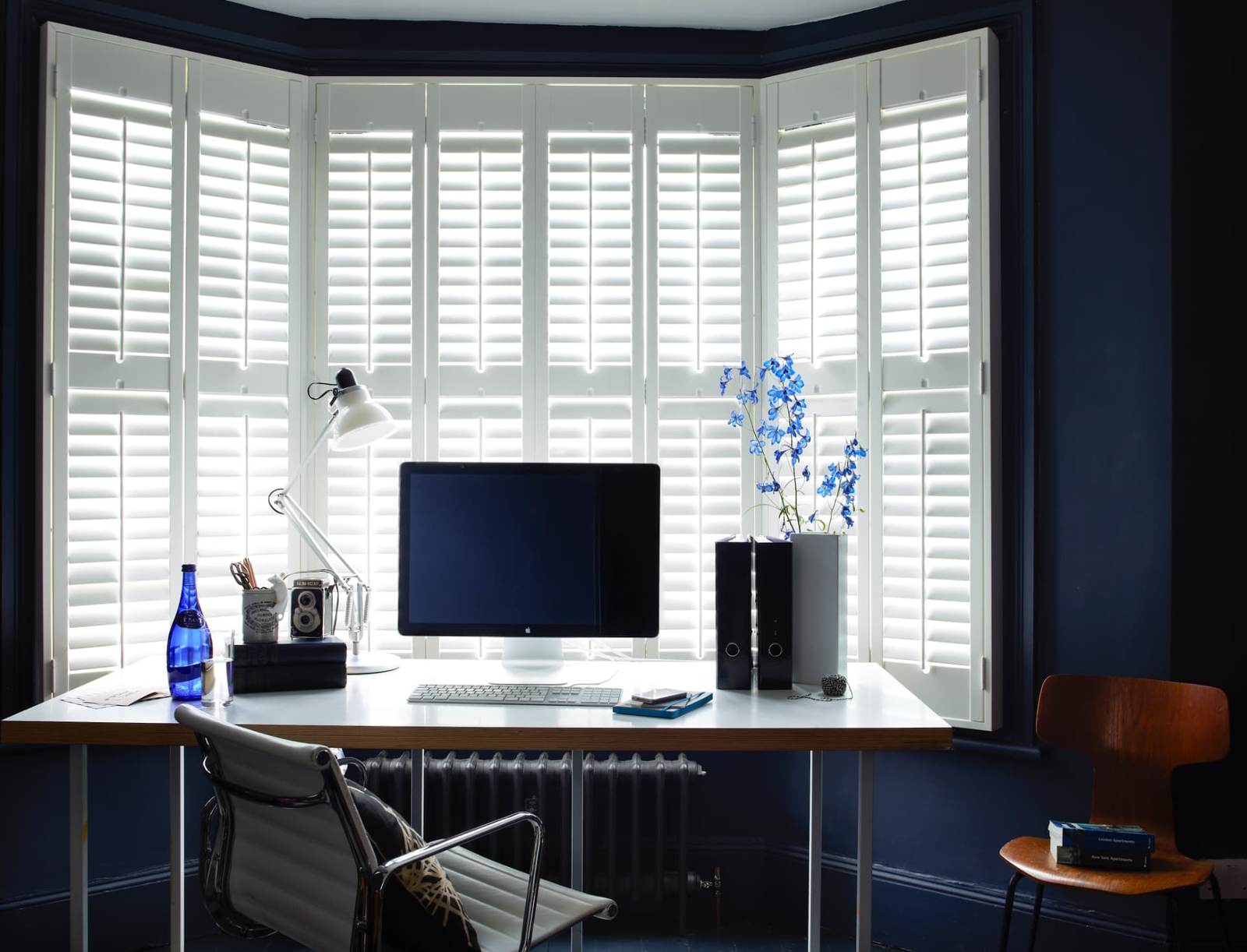 White full height shutters across a bay window in a navy home office