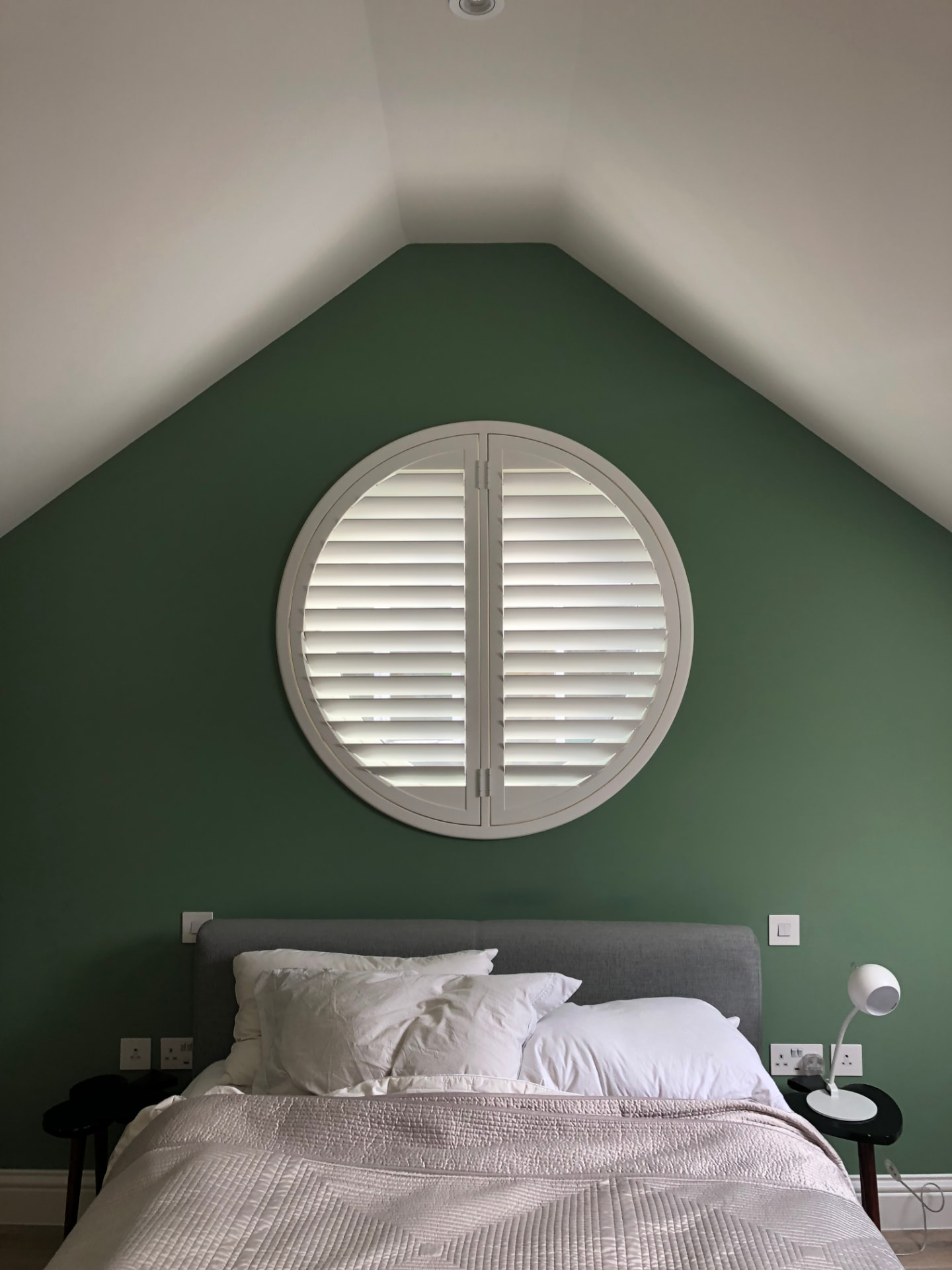Circular shutter with a central T-post in a green loft bedroom