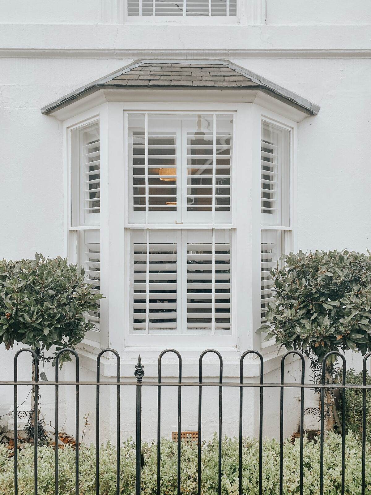 Victorian bay window fitted with white shutters seen from the street