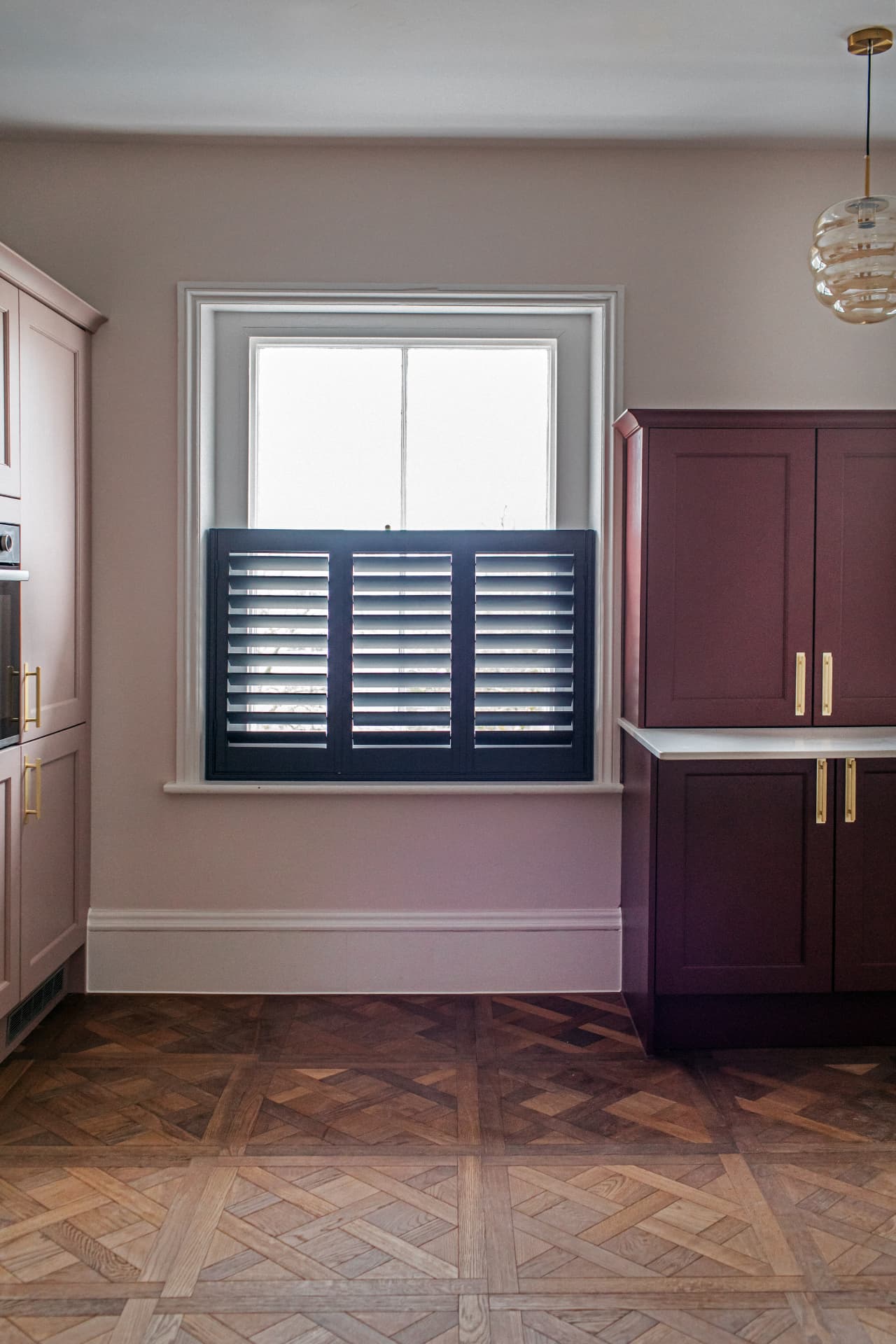 Navy café style shutters with louvres closed in a pink and burgundy kitchen