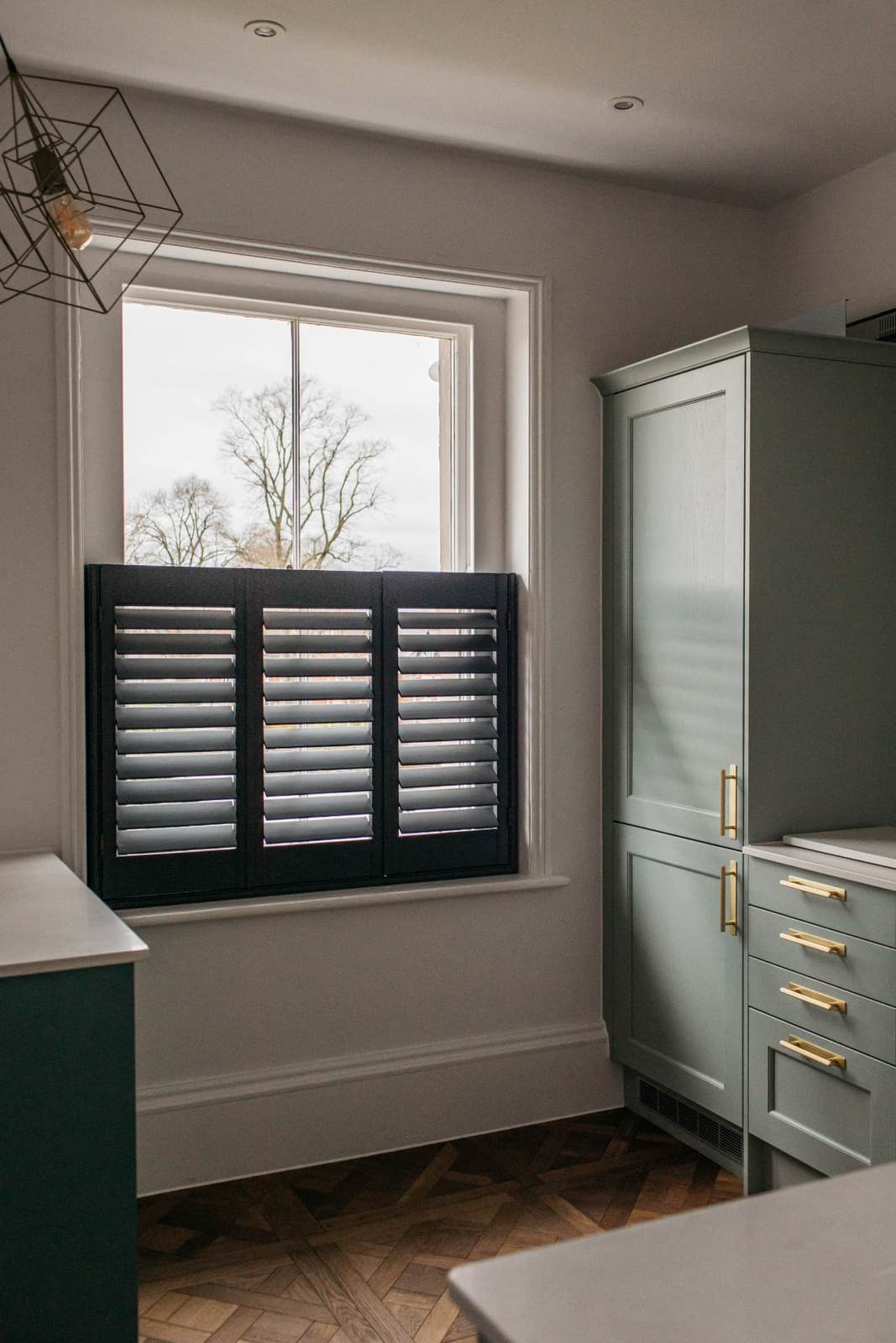 Navy café style shutters with louvres open beside sage green cabinetry