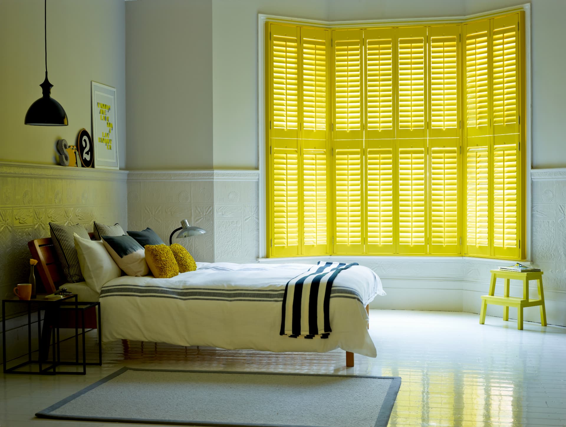 Custom yellow tier-on-tier shutters closed across a bedroom bay window