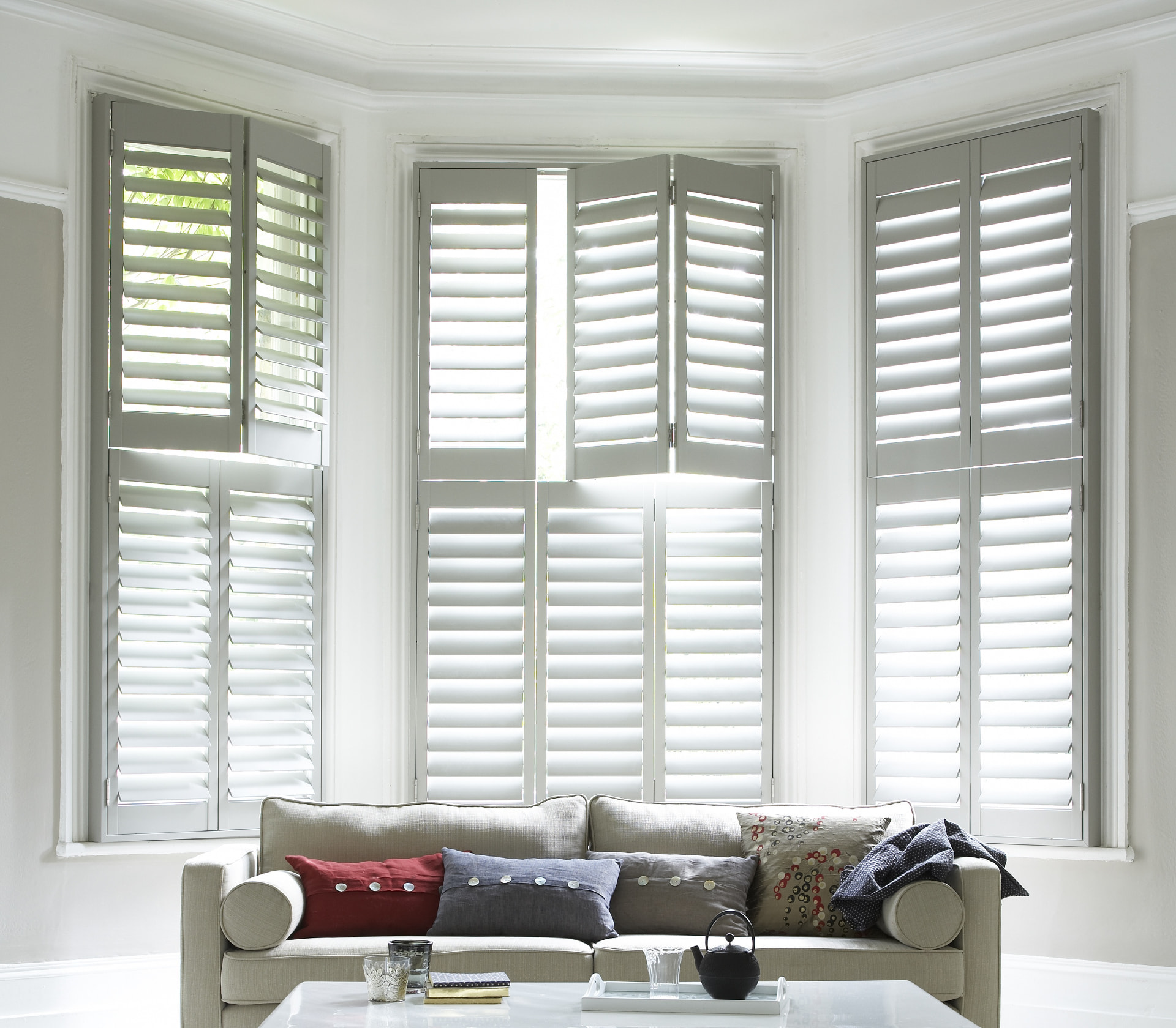 Soft grey tier-on-tier shutters across a Victorian bay window in a white lounge