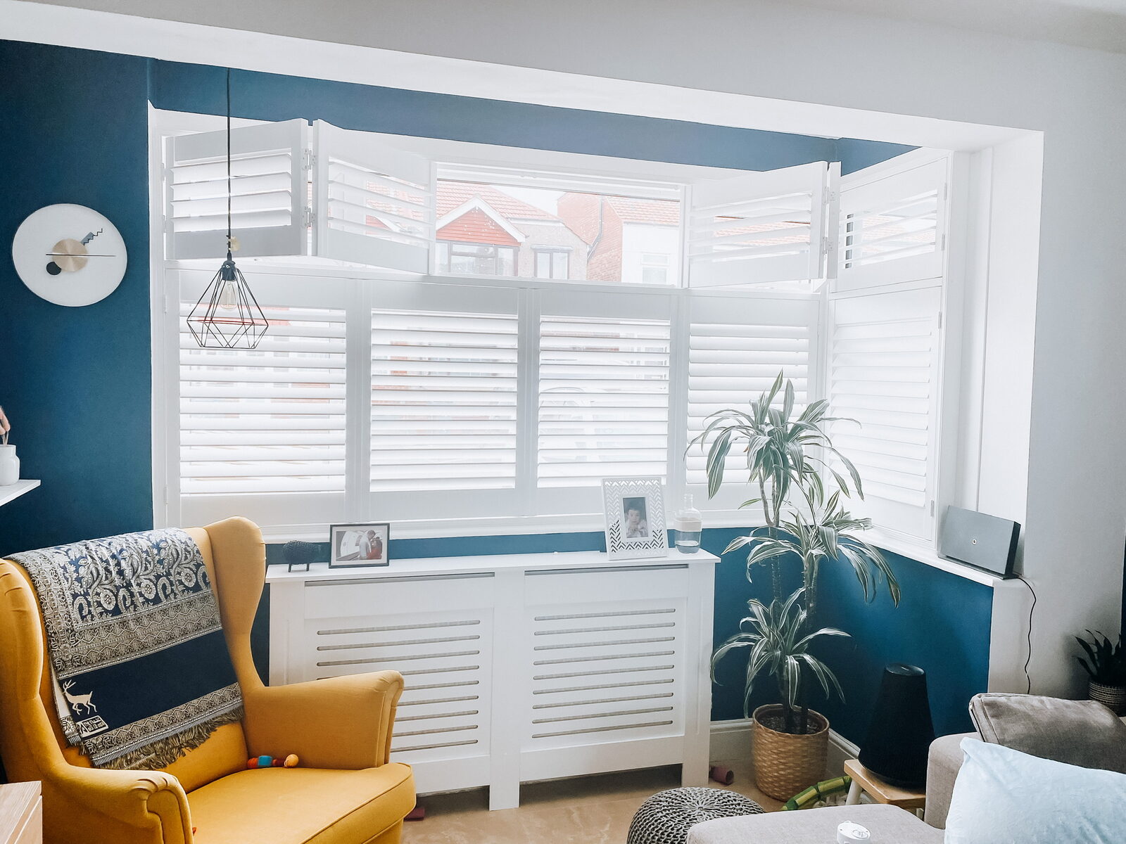 White shutters in a blue living room bay with a yellow armchair
