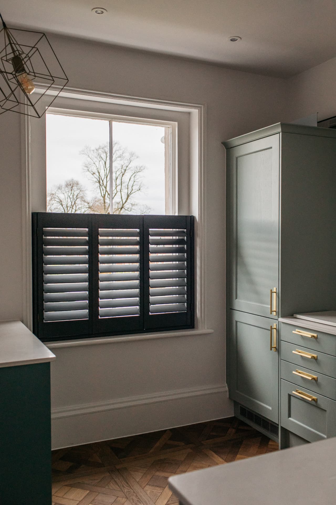 Navy café style shutters with louvres open beside sage green cabinetry
