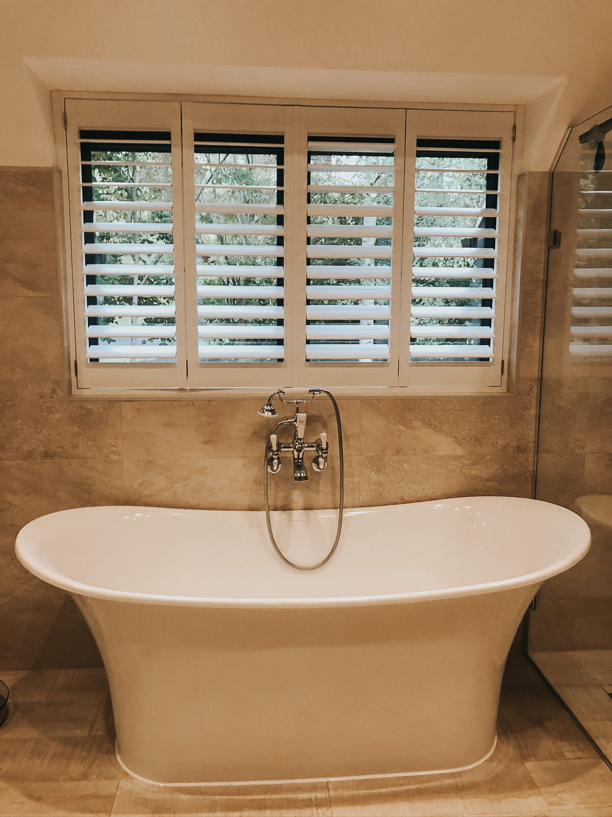 Shutters above a freestanding bath in a stone bathroom