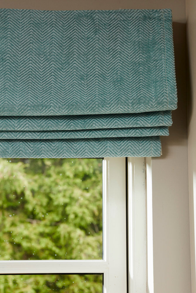 Close-up of a herringbone teal roman blind stacking neatly